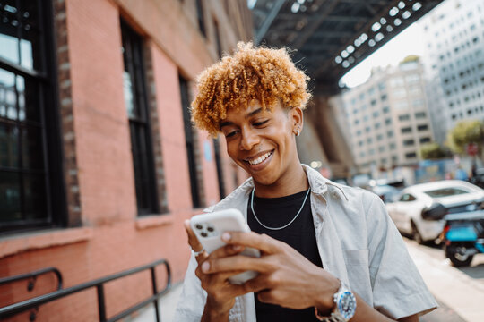 Portrait of young multiracial man smiling happy using smartphone while walking at the city