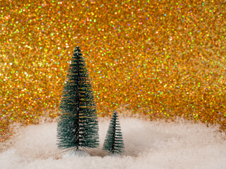 The photo shows a festive scene with decorative artificial Christmas trees set on shiny white snow. The backdrop features a shimmering gold backdrop that adds elegance and magic to the winter wonderla