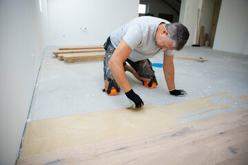 middle-aged man with gray hair glued, laying parquet floor in my loft apartment, top floor