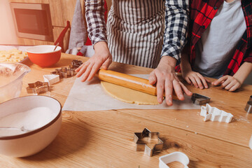 Dad and son at a wooden table in the kitchen are going to make cookies by rolling out the dough with a wooden rolling pin. Top view