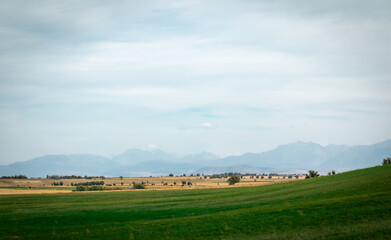 Fototapeta premium green hill against the backdrop of high mountains and storm clouds