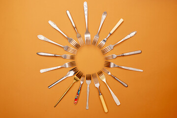 Cutlery. Pop art style. Flat lay of variety of stainless steel, antique silverware and gold forks arranged in circle over orange studio background.