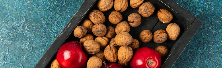 ripe apples and whole walnuts in black wooden tray on blue textured surface, thanksgiving, banner