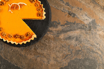 bright thanksgiving pie with walnuts and dried orange slices on black slate table and stone surface