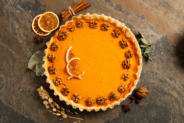 thanksgiving setting, pumpkin pie with walnuts and orange slices near cinnamon sticks on stone table