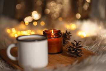 christmas still life with candle. new year christmas card. lights of garlands, lighted candle and a cup of coffee. comfort and hygge. selective focus. bokeh 