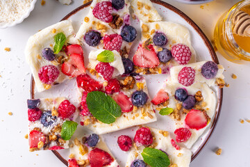 Homemade frozen Yogurt Bark, alternative healthy keto diet ice cream made from greek yogurt, fresh berries, nuts, granola, honey, on baking tray deco. Frozen yoghurt bars with fruit berry toppings