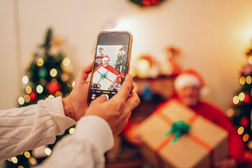 Close up of hands taking picture of his family by smart phone, family, Christmas, technology and selective focus on phone. - obrazy, fototapety, plakaty