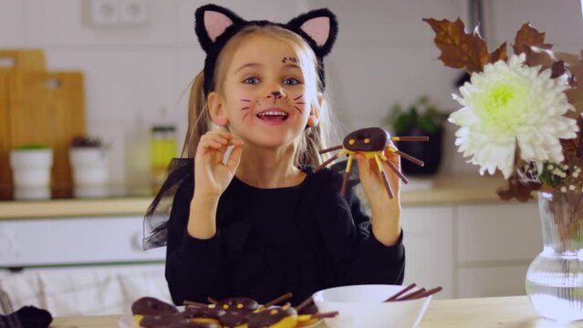 child Halloween costume in the kitchen at home makes donuts with chocolate into spiders, a treat for the holiday, Happy halloween day concept