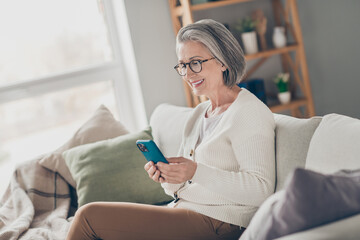 Photo of cheerful charming elderly lady wear white cardigan spectacles texting sms instagram...