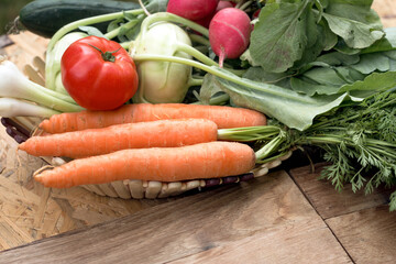 Fresh organic vegetables in a basket on wooden table, healthy vegeterian food close-up 