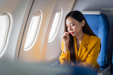 Young asian chinese airplane passenger woman experiencing discomfort, Airplane headache. Worried female passenger holding head, feeling unwell Anxiety and fear in the skies. Stressful travel moments.