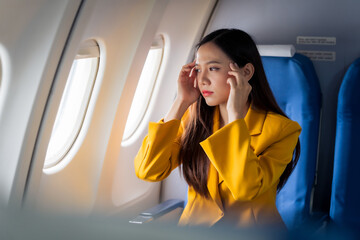 Young asian chinese airplane passenger woman experiencing discomfort, Airplane headache. Worried female passenger holding head, feeling unwell Anxiety and fear in the skies. Stressful travel moments.