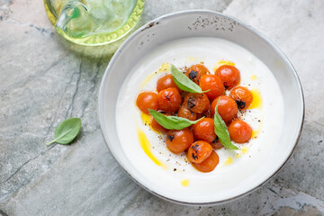 Bowl of greek feta dip with roasted cherry tomatoes and green basil, elevated view on a grey granite background, horizontal shot