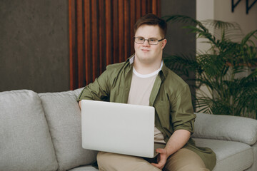 Young IT man with down syndrome wear casual clothes work hold use laptop pc computer sits on grey...