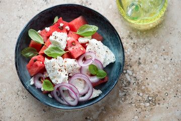 Blue bowl with watermelon and feta cheese salad on a beige granite background, high angle view, horizontal shot