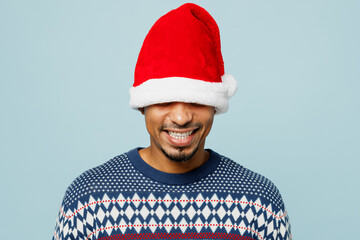 Young smiling rejoicing cheerful fun cool man wear knitted sweater cover eyes with Santa hat posing...