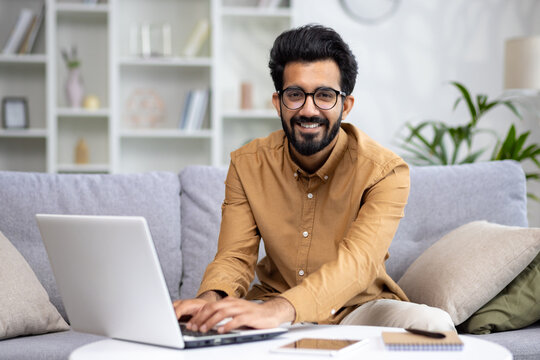 Portrait of young Muslim businessman, freelancer working from home on laptop. Typing on the keyboard and smiling at the camera.