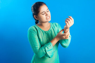 Young caucasian women holding her wrist with painful grimace in blue background.
