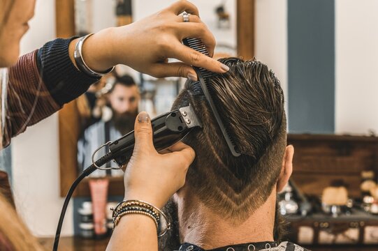 Hipster man at barbershop salon getting beard and hair cut - Hairdresser woman using hair clipper to modern cut with geometric drawing on the nape - Barber shop concept