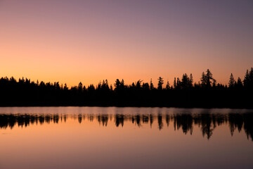 forest silhouette reflected in big lake at sunrise - 664470618