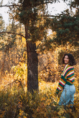 Lady in a striped knitted sweater stands near a tree in the forest.