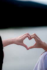 young woman and her friend raised their hands together to form heart shape to show their friendship...