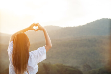 The young woman raised her hands above her head and made a heart shaped sign to show friendship love and kindness towards one another. The concept of friendship love between friends and kindness - obrazy, fototapety, plakaty