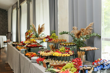catering buffet table with snacks and appetizers. Set of varios fruits and berries. Decorative vase