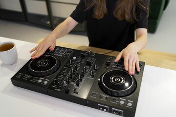 A young woman in black mixes tracks and records a mix with a controller to play in a club later....