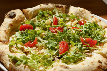 Close-up of a juicy sourdough pizza with arugula and tomatoes in direct sunlight. The concept of delicious food, snacks, culinary recipes