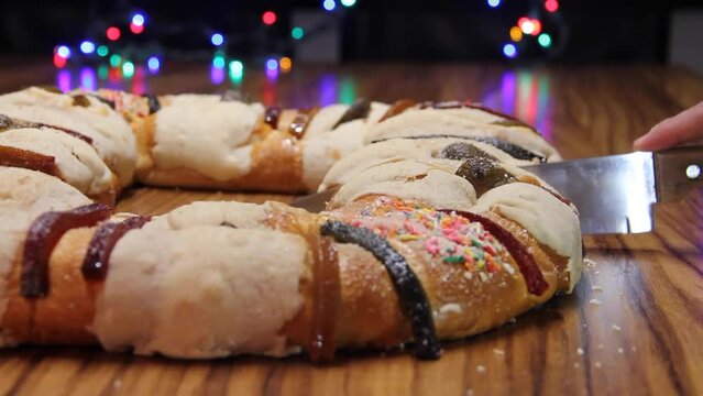 cut the rosca de reyes in foreground on wooden table with out of focus background of colored lights.