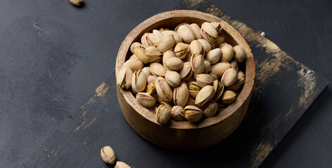 Salted roasted pistachios in a wooden round bowl on the table