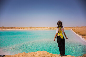Young woman (back view) on the shore of salt lake in Siwa oasis, salty lake with turquoise water, Egypt - obrazy, fototapety, plakaty