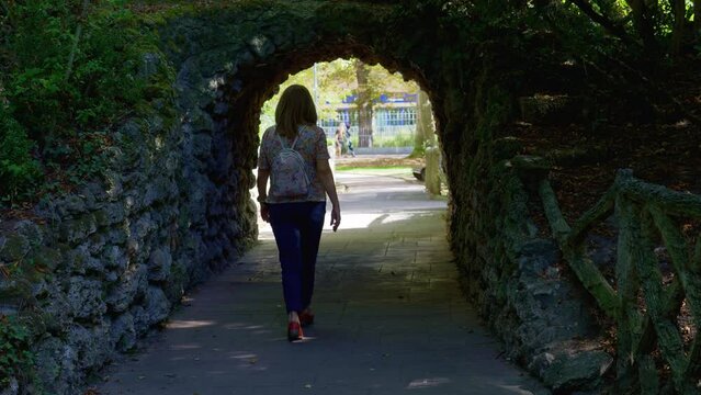 Woman strolling through a public park in a stone tunnel that forms an arch, Vitoria, Spain.