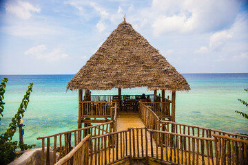 Wooden pavilion with palm leaves roof against turquoise water background, Zanzibar