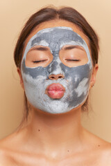 Woman doing cosmetic clay mask for skincare, sending air kiss with closed eyes, daily beauty routine concept, copy space