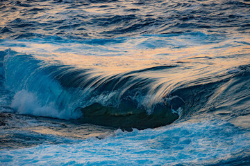 Shorebreak wave hitting a rock in Ikaria with magical colorful sunset lights