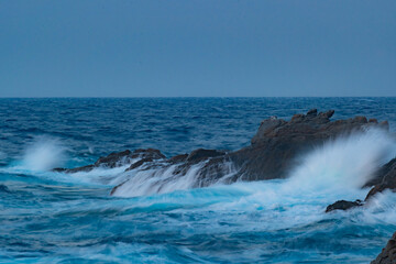 Fototapeta premium Shorebreak wave hitting a rock in Ikaria with magical colorful sunset lights
