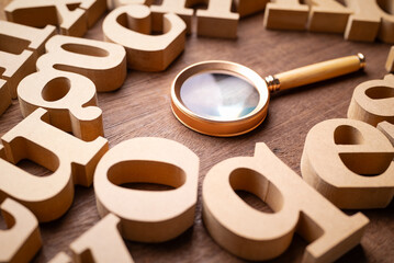 Closeup magnifying glass in the group of wooden English alphabets, glossary, English education, keyword searching, or communication concept