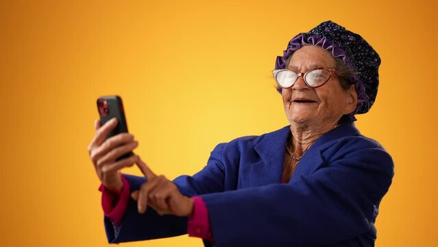 Funny crazy happy elderly old toothless woman talking on mobile cell phone wearing glasses isolated on solid yellow background studio portrait. 