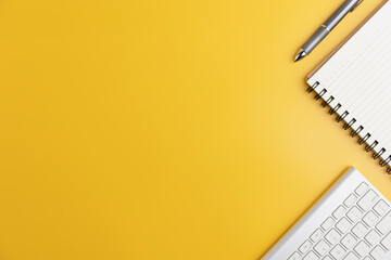 The home office with a pen, and notebook with a mouse on a yellow table with copy space. Top view, flat lay minimal yellow desk concept. Workspace desk with keyboard on yellow background.