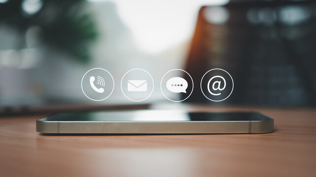 Side view of smartphone resting on wooden table surface with communication icons above representing contact us and marketing and customer support concept.