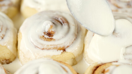 Spreading frosting on cinnamon rolls. Freshly baked homemade cinnamon buns