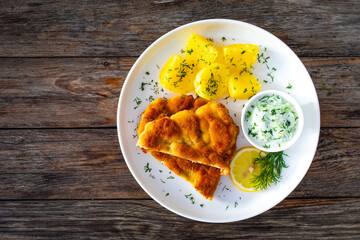 Crispy breaded seared chicken cutlet with boiled potatoes and cucumbers in cream on wooden table
