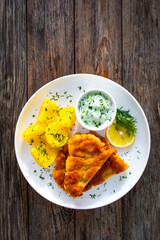Crispy breaded seared chicken cutlet with boiled potatoes and cucumbers in cream on wooden table
