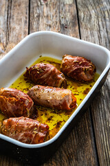 Stuffed pork loin with dried plums wrapped in cured ham in cooking pan on wooden table
