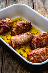 Stuffed pork loin with dried plums wrapped in cured ham in cooking pan on wooden table
