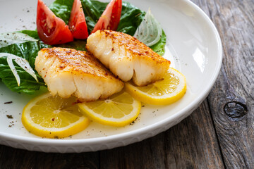 Seared cod loin and fresh vegetables on wooden table
