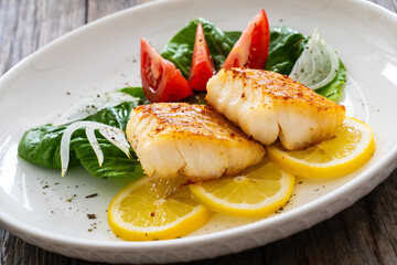 Seared cod loin and fresh vegetables on wooden table
